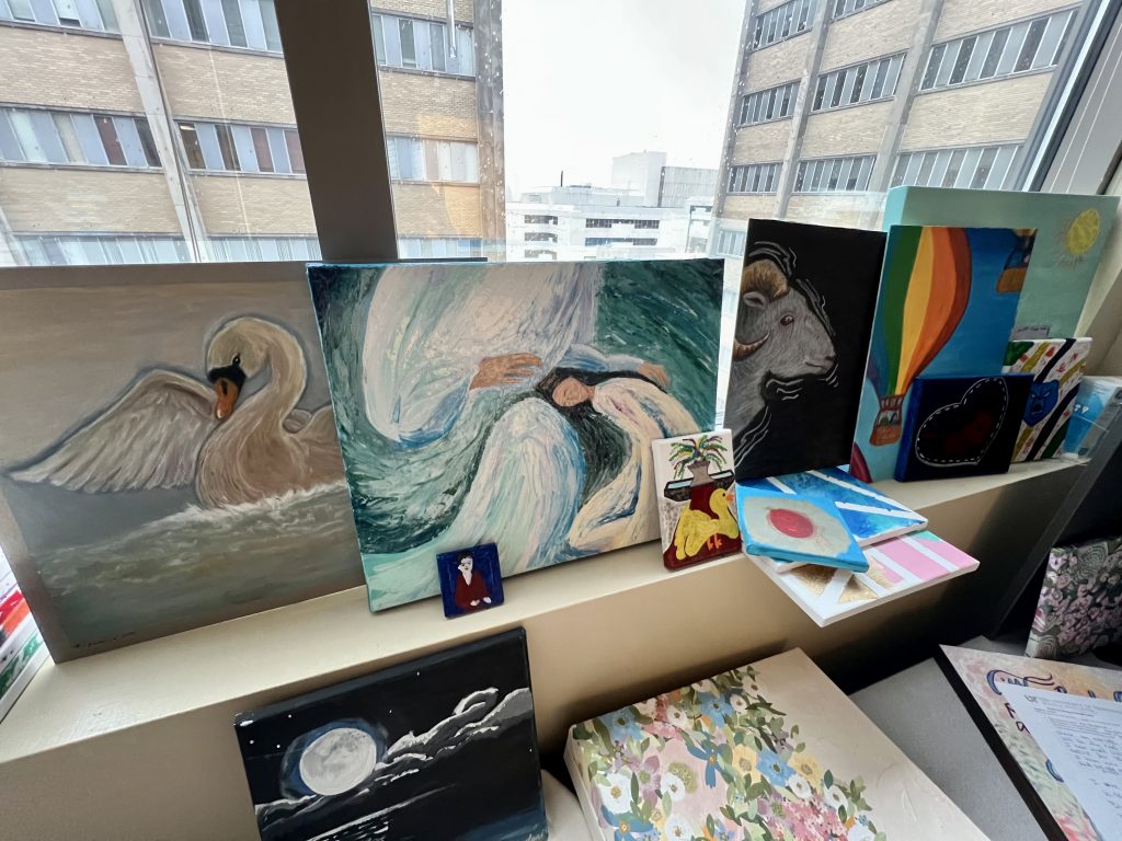 Various paintings are set up in front of an office window overlooking the city