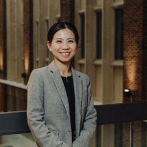 Dr. Huang standing in a blazer against a railing in a building