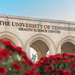 The University of Tennessee Health Science Center letters over stone arches, with red flowers in the foreground