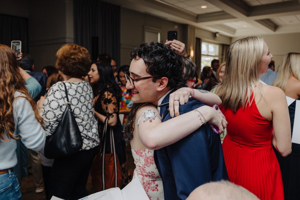 Medical student Ben Finder embraces a young woman in a flowered dress. She has a medical device on her arm.