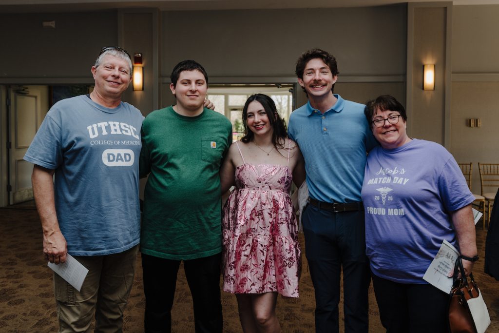 A group of five loved ones pose for a photo, the two parents wearing UTHSC College of Medicine parent T-shirts.