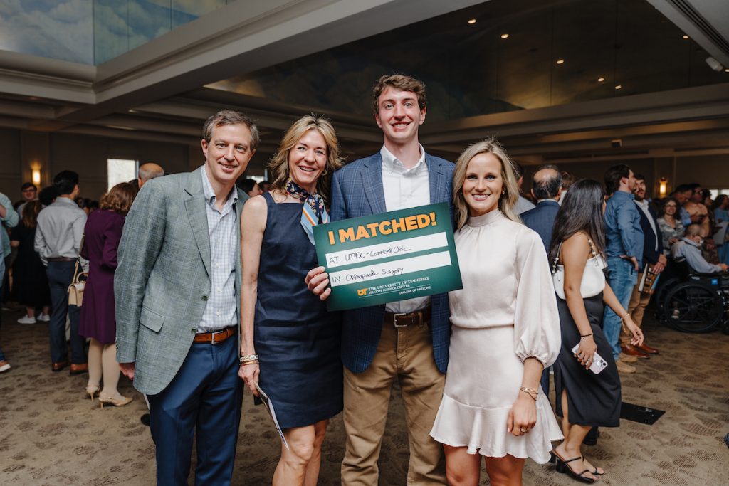 A tall student with his loved ones, holding his "I Matched!" sign that reads "at UTHSC - Campbell Clinic in Orthopoedic Surgery."
