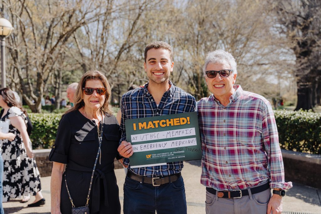 A student with his relatives outdoors, holding his "I Matched!" sign that reads "at UTHSC - Memphis in Emergency Medicine! GO TIGERS!"