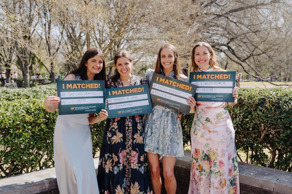 A group of young women in dresses pose for a photo outside on a patio with shrubs and trees behind them, holding their "I Matched!" signs. Their details include Saint Louis University in OB/GYN, University of Utah in Dermatology, UTHSC Memphis in Pediatrics, NCC A.T. Augusta Military MC in Family Medicine.