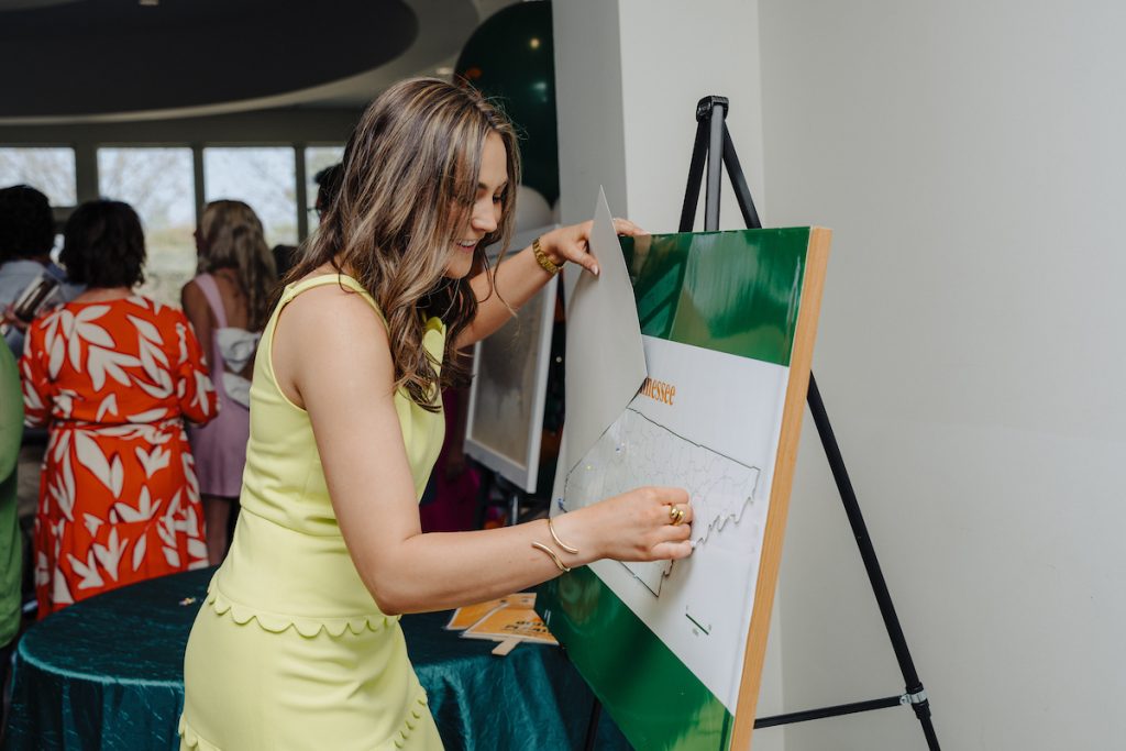 A young woman student in a yellow dress pins where she's going to a board showing the state of Tennessee.