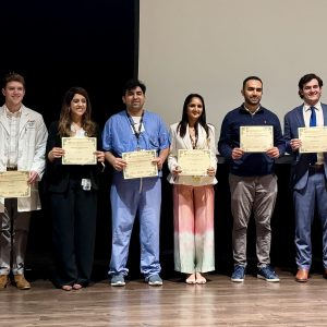The Research Day award recipients standing on a stage between the organizers and holding their certificates.