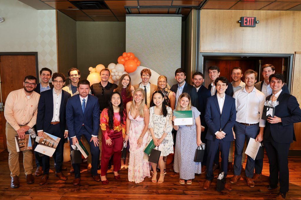 A group of young men and women dressed up and some holding envelopes pose inside in front of orange and white balloons on Match Day in Knoxville.