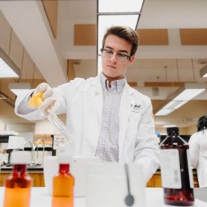 A College of Pharmacy student pours medicine into a container in a lab.
