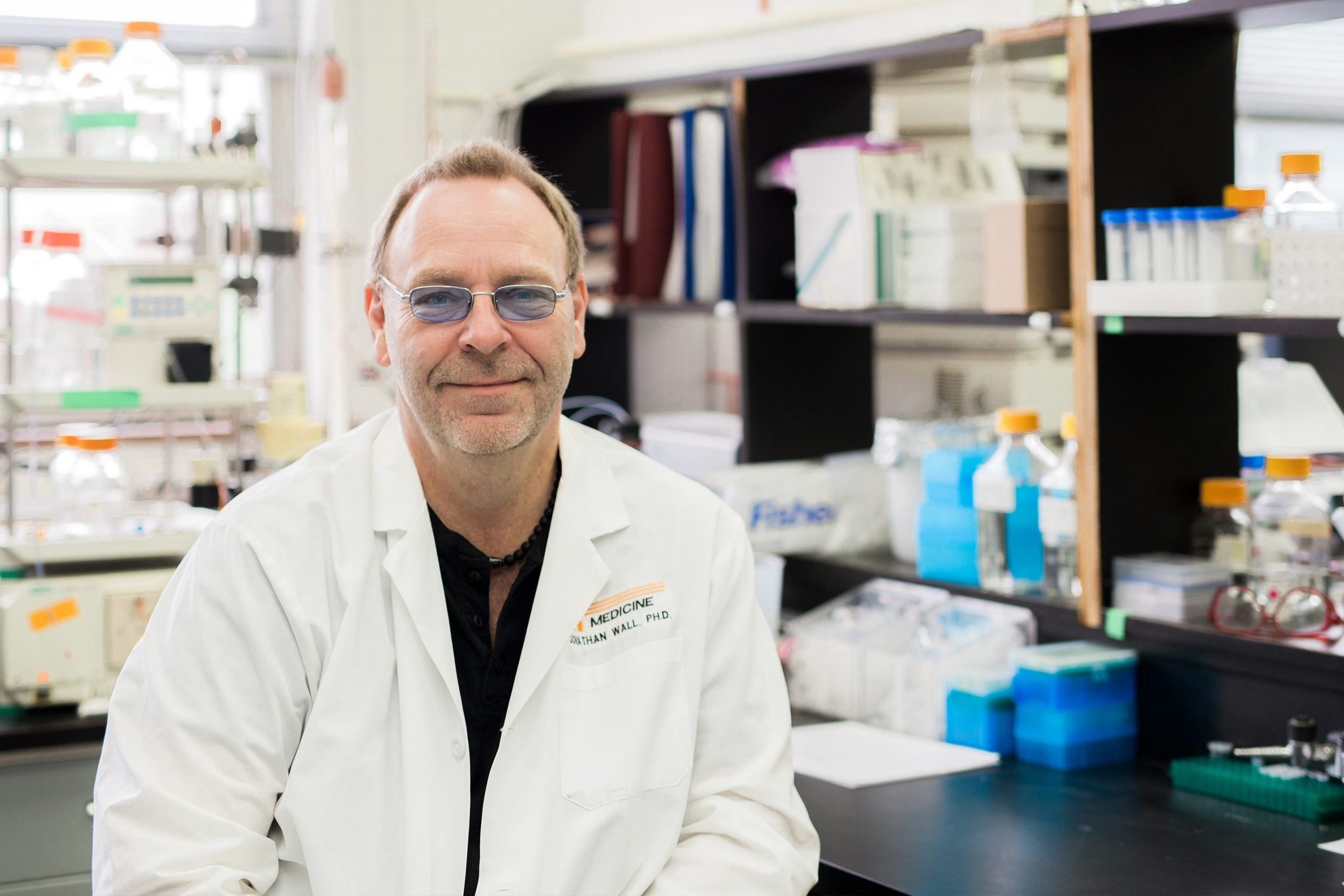 Portrait of Dr. Jon Wall sitting in a lab in front of shelves containing scientific instruments and materials