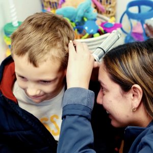 An audiology student looking into a young patient's ear
