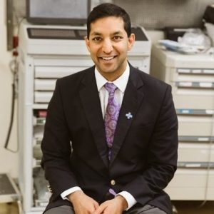 Dr. Dave Battacharya sits in a room with medical equipment.