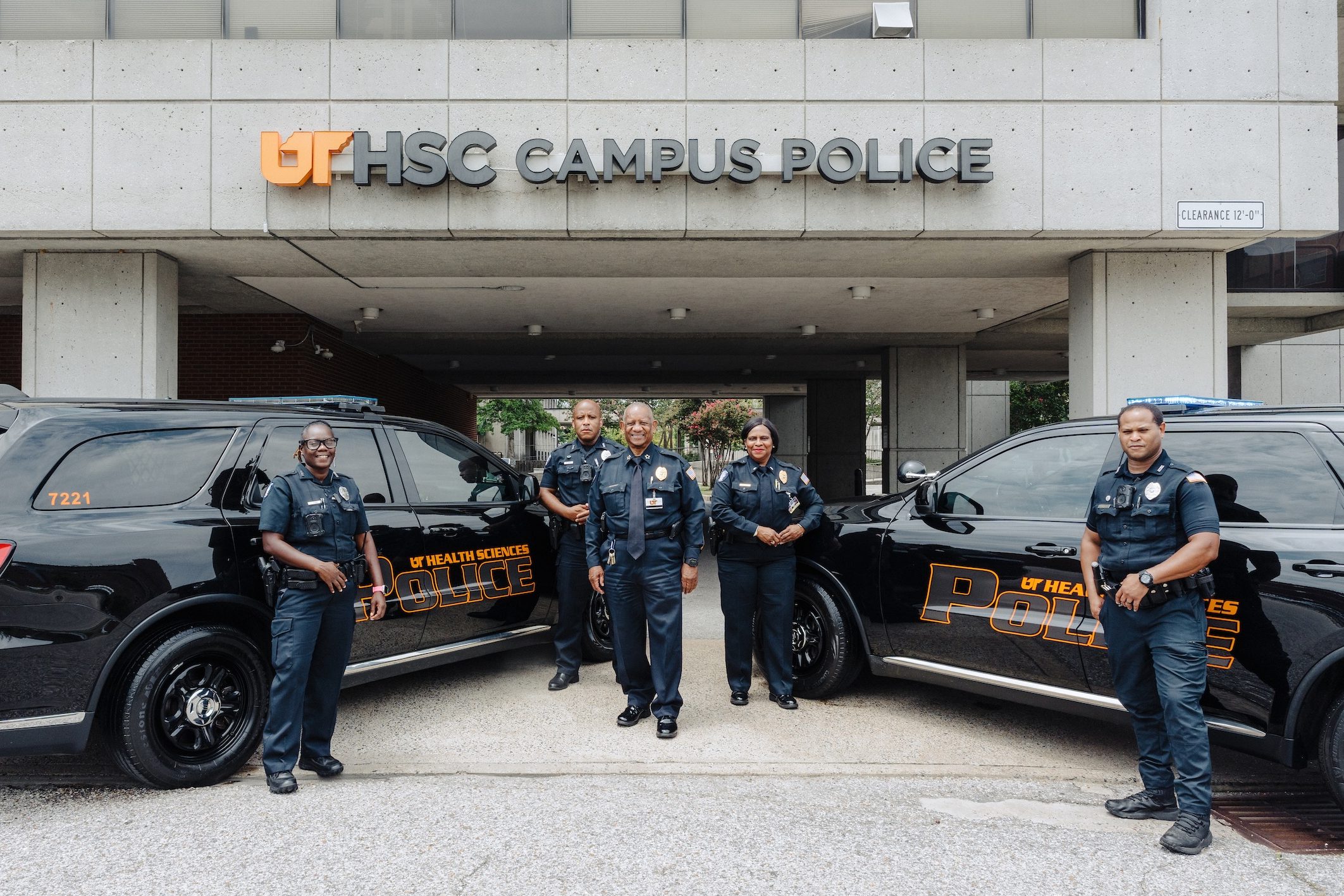 Five campus police officers standing in front of two new squad cars
