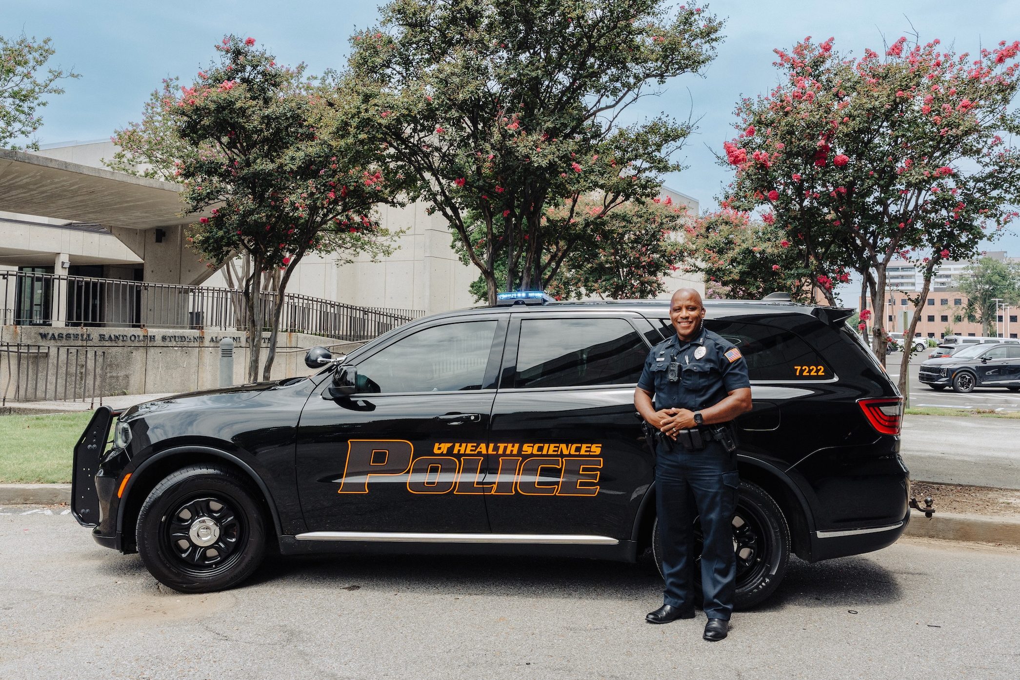 A campus police officer standing in front of a new squad car, which is black with orange writing that reads "UT Health Sciences Police"