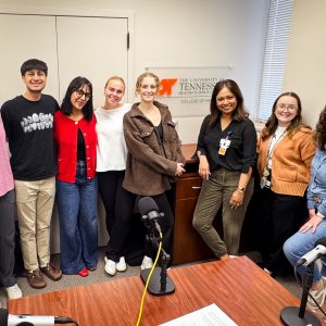 Dr. Faria Abdullah with her podcast team, the podcast table in the foreground and a UT Health Sciences College of Medicine sign in the background.