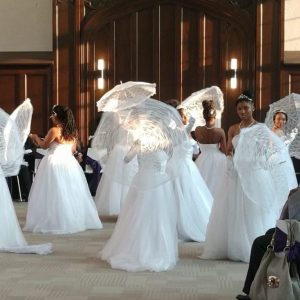 Girls in white dresses twirl with umbrellas