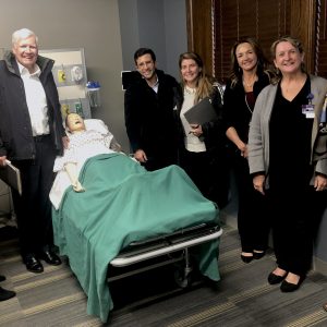 The participants on a recent tour of a UT Health Sciences College of Nursing simulation suite. The participants are gathered around a simulation mannequin patient in a hospital bed.