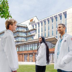 College of Medicine students stand in front of the future site of the College of Medicine Interdisciplinary Building, with a rendering of the building in the background.
