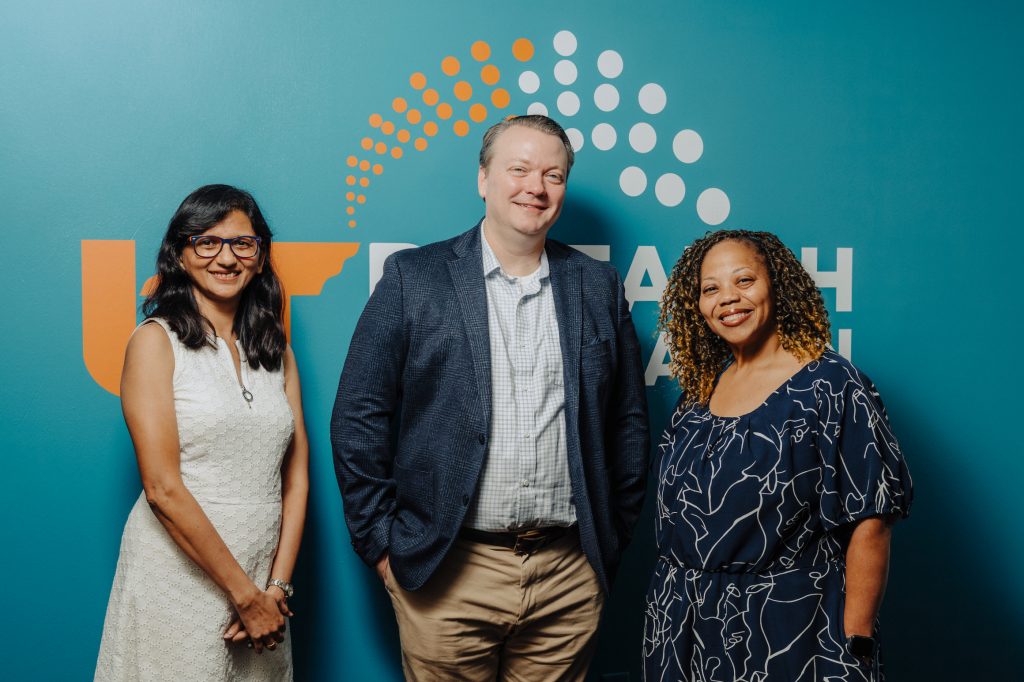 Tulika Rastogi, Dr. James Parrett and Tinieka Thrailkill pose in front of a wall with a UTRF design