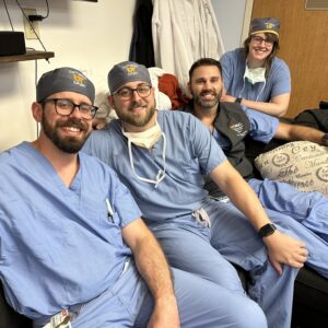 Dr. Chace Hicks and fellow residents in UT Health Sciences scrubs sit together on a couch at work.
