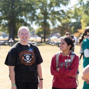 A student wearing a UT Doctors throwback T-shirt smiles at the camera while outside on a field with fellow students.